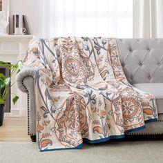 a couch with a blanket on it in front of a window and potted plant