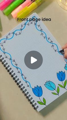 someone is drawing flowers on a notebook with markers and crayons in the background