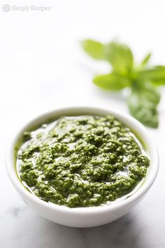 a white bowl filled with green pesto on top of a table next to a sprig of basil