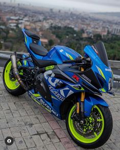 a blue and yellow motorcycle parked on top of a brick road next to a city