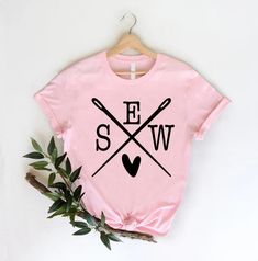 a pink t - shirt with two crossed baseball bats on it and the word ew in black