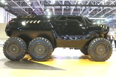 an suv is on display in a showroom with people looking at the vehicle and it's big tires