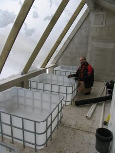 a man standing next to some white containers in a room with skylights on the ceiling