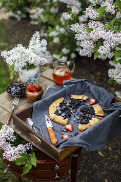 a table topped with a pie covered in blueberries and strawberries next to flowers