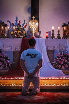 a man sitting on the ground in front of a church altar with candles and flowers