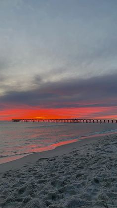 the sun is setting over the ocean with a pier in the distance