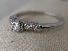 an engagement ring with three stones on it sitting on top of a cushioned surface