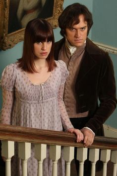 a man and woman standing next to each other on a stair case in front of a painting