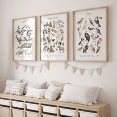 three framed pictures hang on the wall above a bench filled with pillows and other items