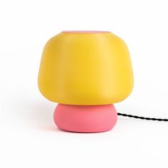 a yellow and pink lamp sitting on top of a white table next to a black cord