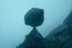 a rock balanced on top of another rock in the middle of a foggy mountain