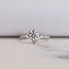 a white gold ring with a single diamond on the side, sitting on a table