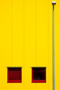 two windows on the side of a yellow building with a street light in front of them