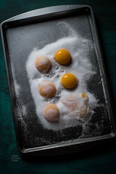 three eggs are sitting on top of flour in a baking pan with one egg broken