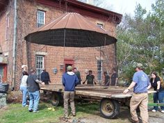 several people standing in front of a brick building with a large flat bed on it