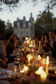 a group of people sitting around a dinner table with candles on it and plates in front of them