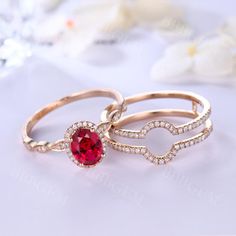 two gold rings with an oval shaped ruby stone surrounded by smaller round diamonds on a white surface