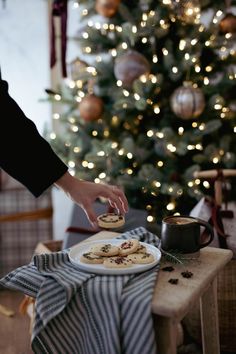 a person is decorating cookies on a table in front of a christmas tree with lights