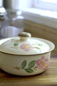 a white casserole with pink flowers on it sitting on a wooden counter top