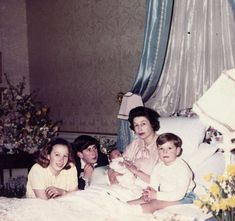 an old photo of three women and two children sitting on a bed with flowers in the background