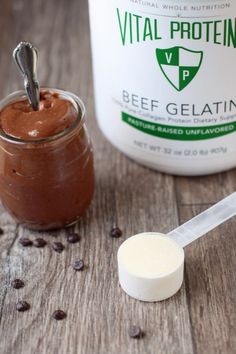 a jar of bee gelatin next to a spoon and chocolate beans on a wooden table