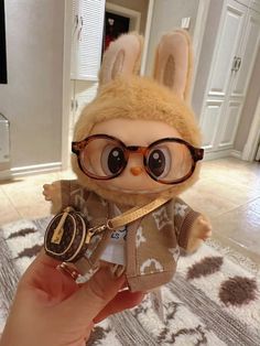 a hand holding a small stuffed animal with glasses on it's head and wearing a jacket