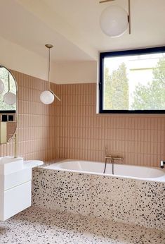 a bath tub sitting under a large window next to a sink and mirror in a bathroom