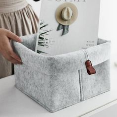 a woman is holding a book in a storage bin on a counter top with a hat