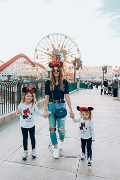 a woman and two children wearing minnie mouse ears walking down a sidewalk in front of a ferris wheel