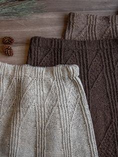 three knitted sweaters and two pine cones on the floor next to each other