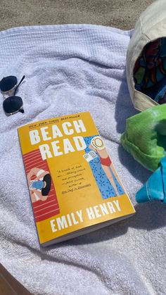 the beach read book sits on a towel next to sunglasses and a stuffed animal toy