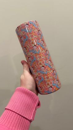 a person holding up a pink and blue patterned paper tube in their left hand, against a gray background