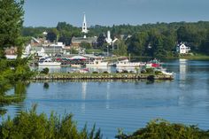 boats are docked on the water in front of some buildings and trees with a church steeple in the background