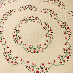 an embroidered tablecloth with red flowers and green leaves on white fabric, in the shape of a circle