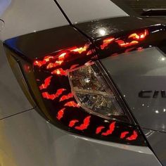 the tail lights of a silver car with red flames on it's grills