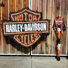 an orange and black harley davidson motorcycle sign next to a fence with two motocycles on it