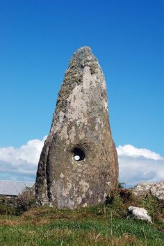 a large rock sitting on top of a lush green field next to a blue sky