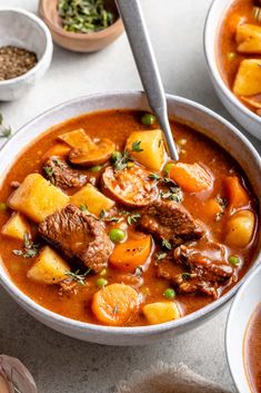 two bowls of stew with meat, potatoes and carrots on the table next to other dishes