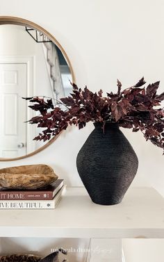 a black vase sitting on top of a white shelf next to a mirror and books