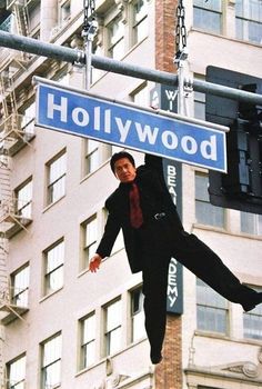 a man hanging from a street sign in front of a tall building with the word booowly ho written on it