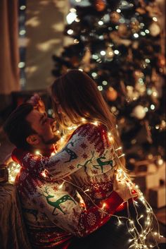 a man and woman are sitting in front of a christmas tree with lights on it