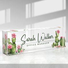 a clear box with pink flowers and green cactuses on the front is sitting on a table