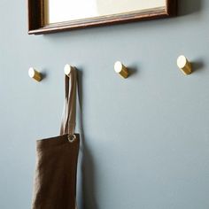 a brown bag hanging on the wall next to a mirror and coat rack with three brass knobs