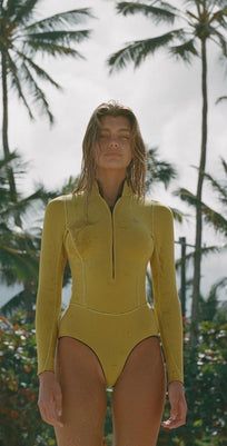 a woman in a yellow swimsuit standing on the beach with palm trees behind her