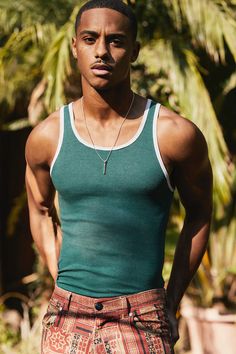 a young man is standing in front of some palm trees and wearing a green tank top