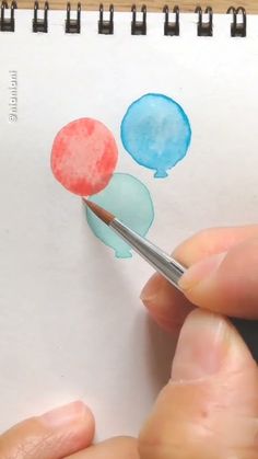 a person is holding a pencil and drawing with watercolors on paper that has balloons