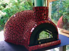 a red brick oven sitting on top of a table next to a window with trees in the background