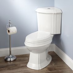 a white toilet in a bathroom next to a roll of toilet paper on the floor