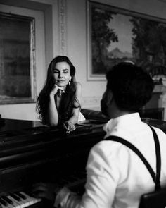 a woman sitting at a piano with a man standing next to her looking at her