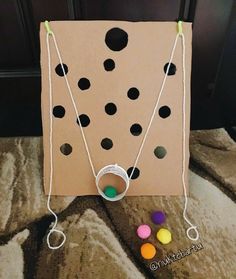 a cardboard board game with several pieces of string and beads attached to it, sitting on a carpeted surface